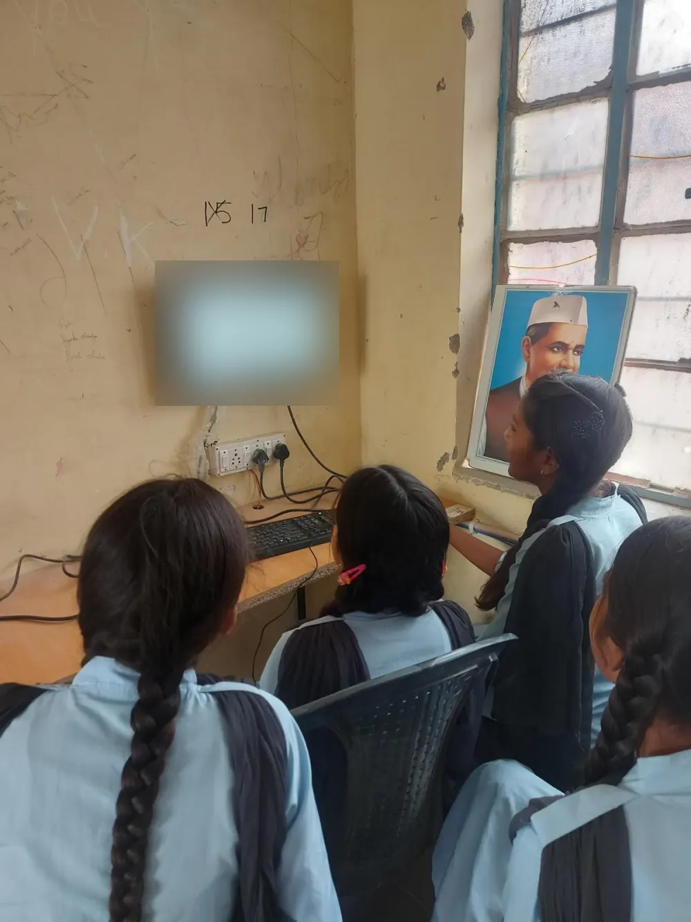 Students in school uniform at a classroom computer, seen from behind.