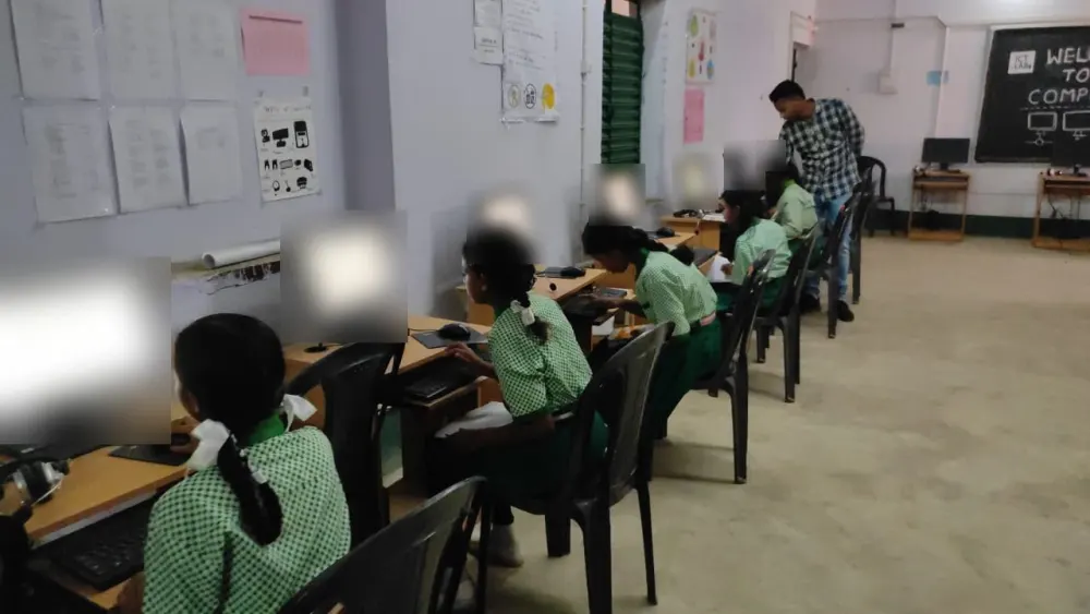 Students in green uniforms at a row of computers, with a teacher at the back of the lab.